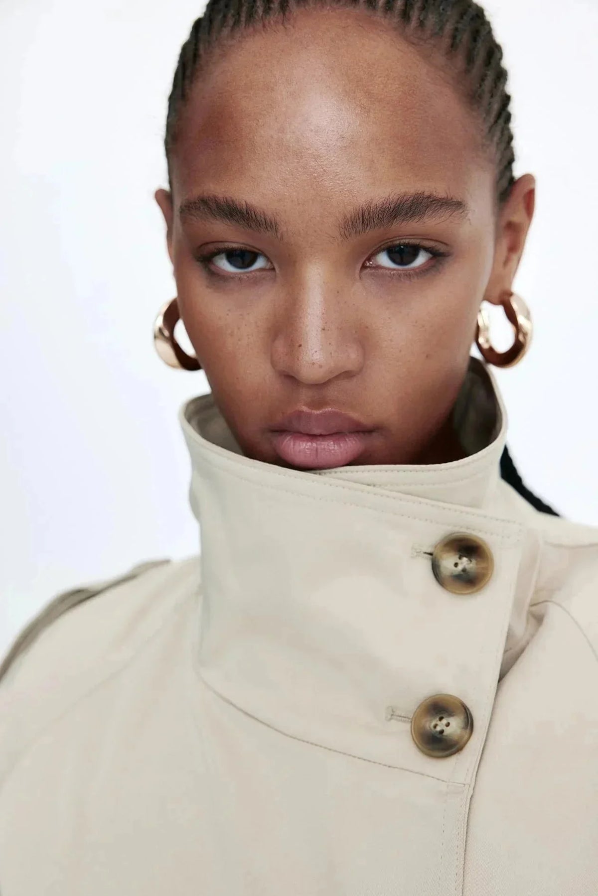 Trench-coat femme beige, col montant, coupe cintrée avec ceinture nouée à la taille.